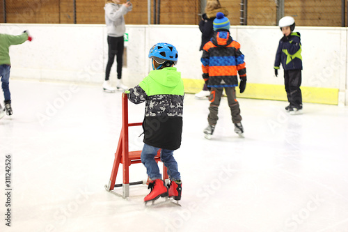 a boy learns to skate with the help of a red chair and is wearing a helmet.