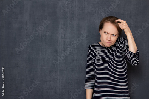 Portrait of funny thoughtful focused girl scratching head with finger