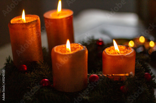 Advent wreath with lighted gold candles and decorated with red berry decorations and with candle flame extinguisher..