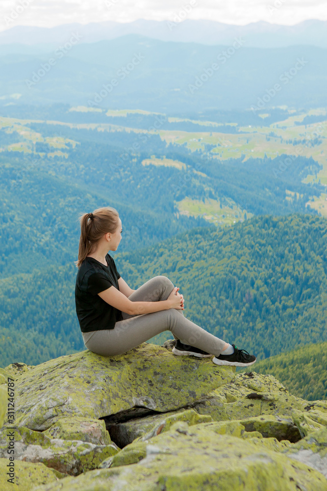 Naklejka premium Young woman sitting on a rock and looking to the horizon.