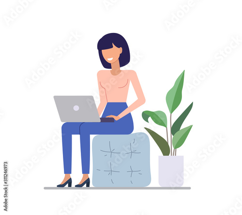The woman is working on the laptop, sitting on a poof in coworking space.
