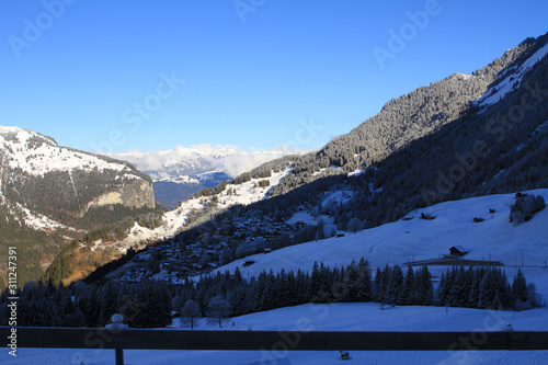 A viewpoint from atop the Swiss Alps, absorbing the mountainous landscape with snow, trees and cabins in a nearby village