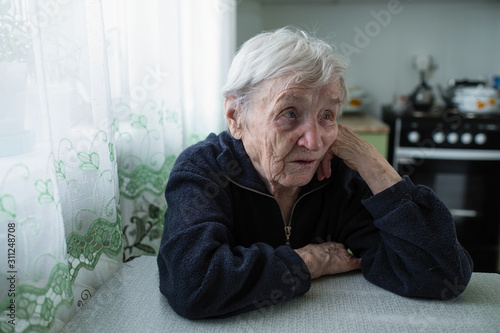 An old woman sitting in the kitchen of her apartment.