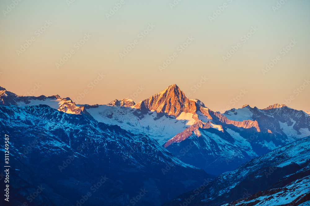 Beautiful nature landscape of Swiss Alps in sunlight rays. Sunset mountains covered with snow in Switzerland. Great view of the snowy rocks and sun beams in Alpine ski resort. Winter holidays.