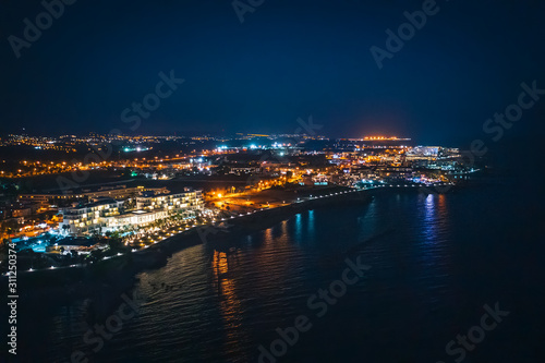 Aerial panoramic view of Paphos, Cyprus seaside from above at night from drone. Beautiful evening mediterranean seascape with illuminated buildings and reflections of lights in sea water