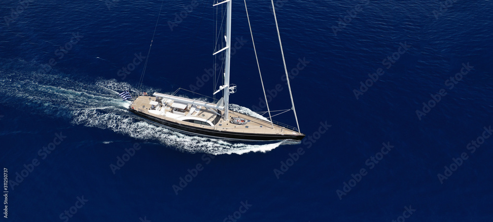 Aerial drone ultra wide photo of beautiful sail boat with wooden deck cruising in open ocean deep blue sea