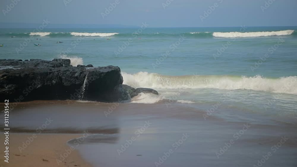 Tropical beach. Big wave crushing coast. Surfers swim in the ocean. Power of water breaking over dangerous rocks. Glassy droplets of water shine in the summer sun. Ocean lifestyle and extreme sports. Tropical beach. Big wave crushing coast. Surfers swim in the ocean. Power of water breaking over dangerous rocks. Glassy droplets of water shine in the summer sun. Ocean lifestyle and extreme sports.