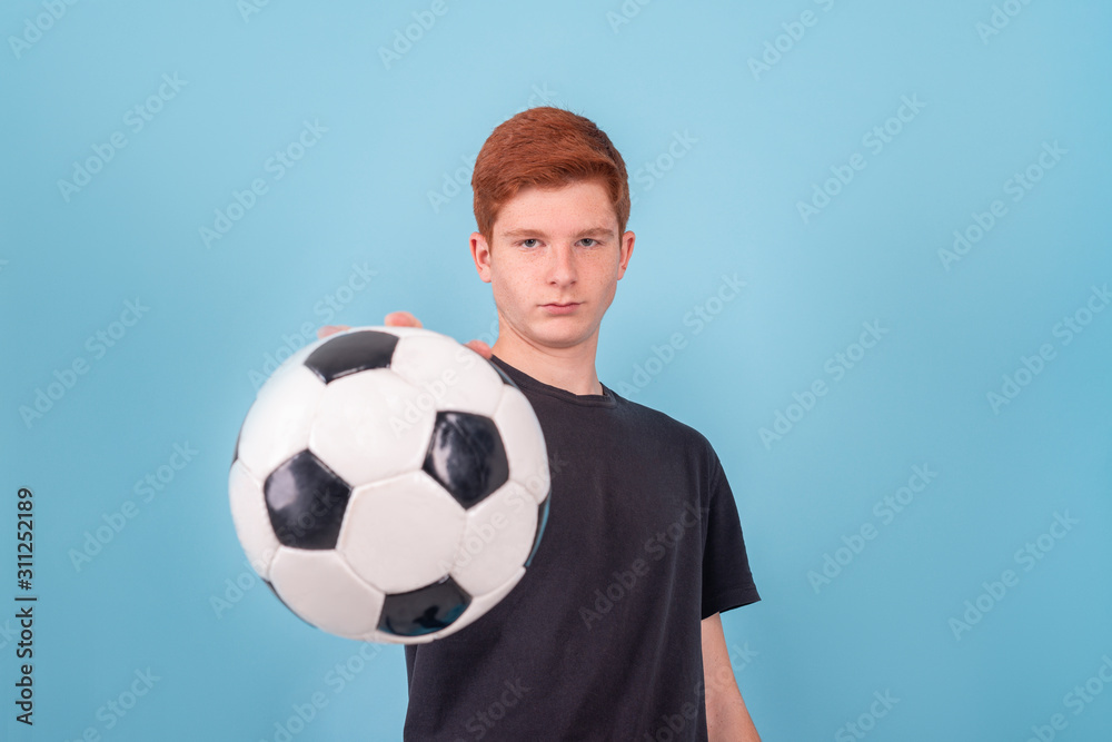 Shot of a red-haired teenager holding a soccer ball in his hand on a blue background. Shot of a red-haired teenager holding a soccer ball in his hand on a blue background.
