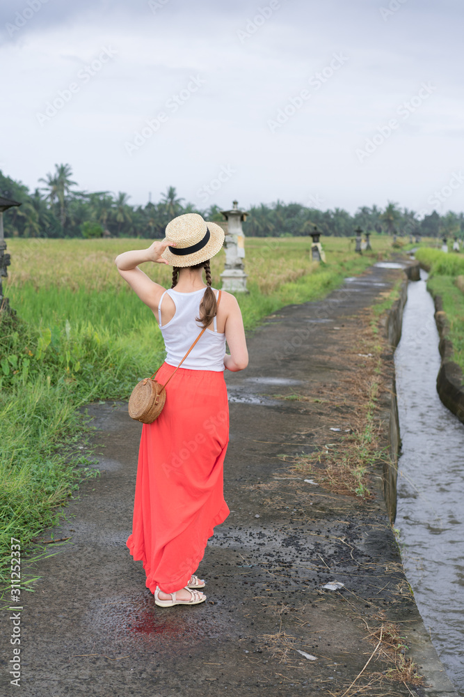 Beautiful young woman in red long maxi skirt with  straw hat and bag. Girl travel in Ubud, Bali, Indonesia