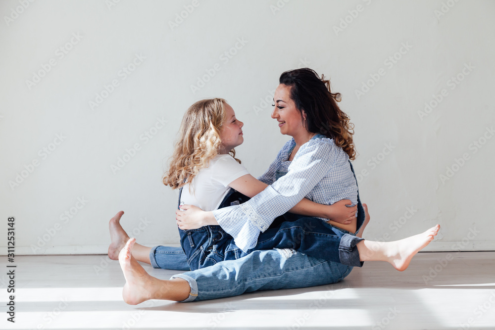 Mom with little girl in denim jumpsuit play in white room Mom with little girl in denim jumpsuit play in white room