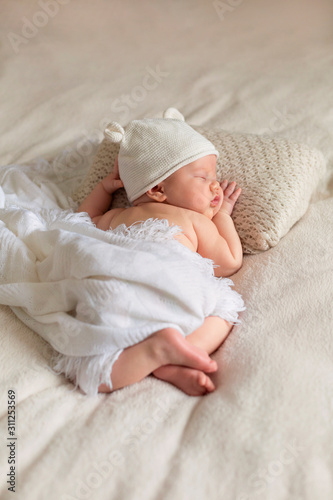 Portrait of cute sleeping newborn baby in white knitted hat in light bedroom. Family, motherhood, love, health, innocence and care