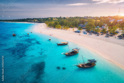 Fototapeta Naklejka Na Ścianę i Meble -  Aerial view of the fishing boats on tropical sea coast with white sandy beach at sunset. Summer holiday on Indian Ocean, Zanzibar. Landscape with boat, palm trees, transparent blue water. Top view