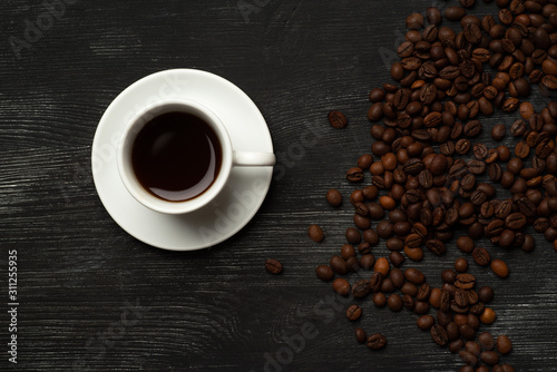 White cup with coffee on a black background with coffee beans and place for text top view