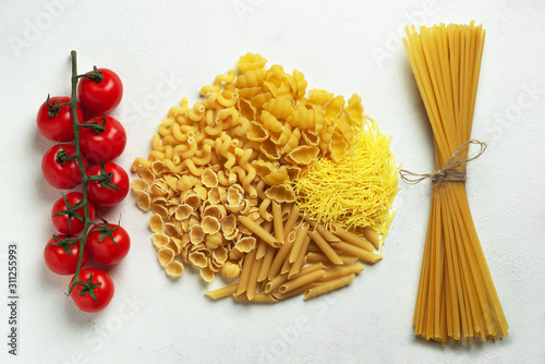 Different types of pasta shells long noodles and raw spaghetti and cherry tomatoes top view