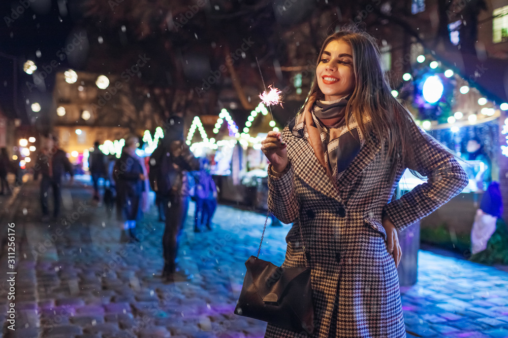 Christmas, New Year concept. Woman burning sparkler on city street fair in Lviv. Girl having fun outdoors on holidays