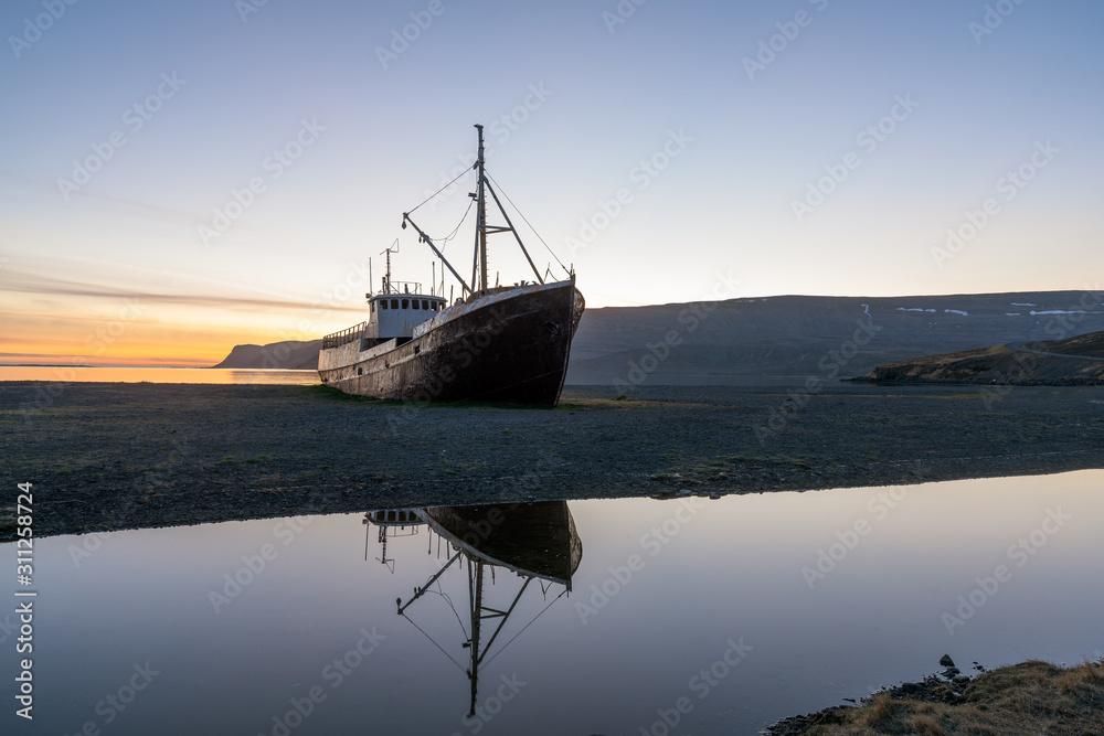 Old ancient, destroyed and abandoned norwegian whaling ship laying ashore in the westfjords of Iceland during sunset. Boat reflects in water. Shipping, whaling and icelandic traveling concept.