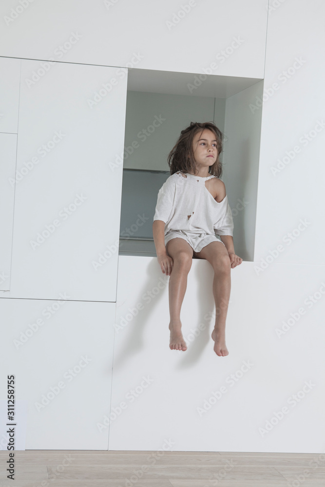 Little girl seated in a hole in a nice apartment wears an old and broken T-shirt Little girl seated in a hole in a nice apartment wears an old and broken T-shirt