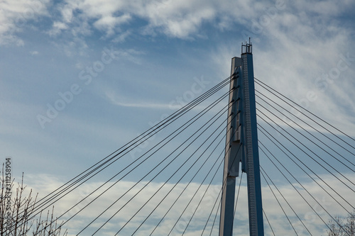 Pylon and steel cables of a suspension pedestrian bridge against a blue sky. Remind a web.