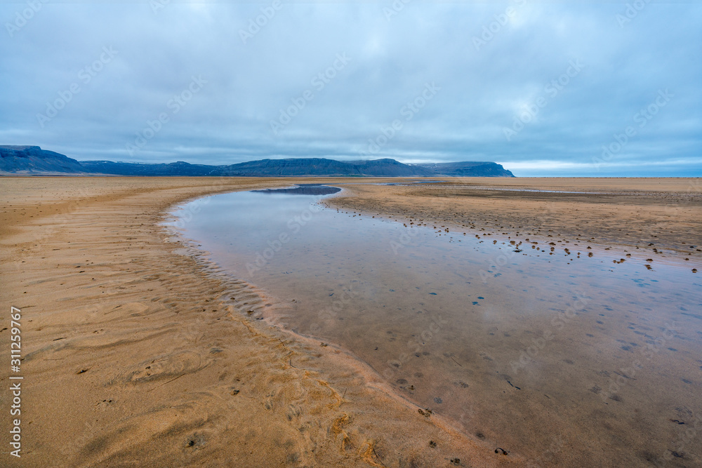 Raudasandur or red sandy beach in the westfjords of Iceland during blue hour. Waves crash into the red sandy dunes at low tide. Texture in the foreground and mountains in the background. 