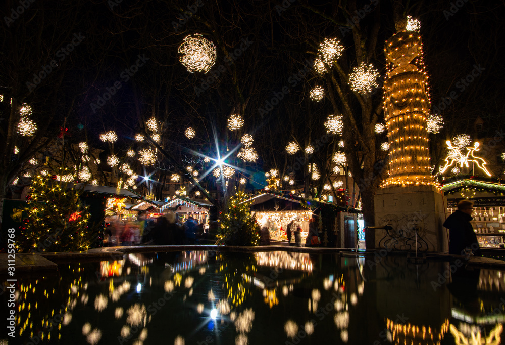 Weihnachtsmarkt in Basel im Dunkeln. Die ganzen Lichter spiegeln im Brunnen
