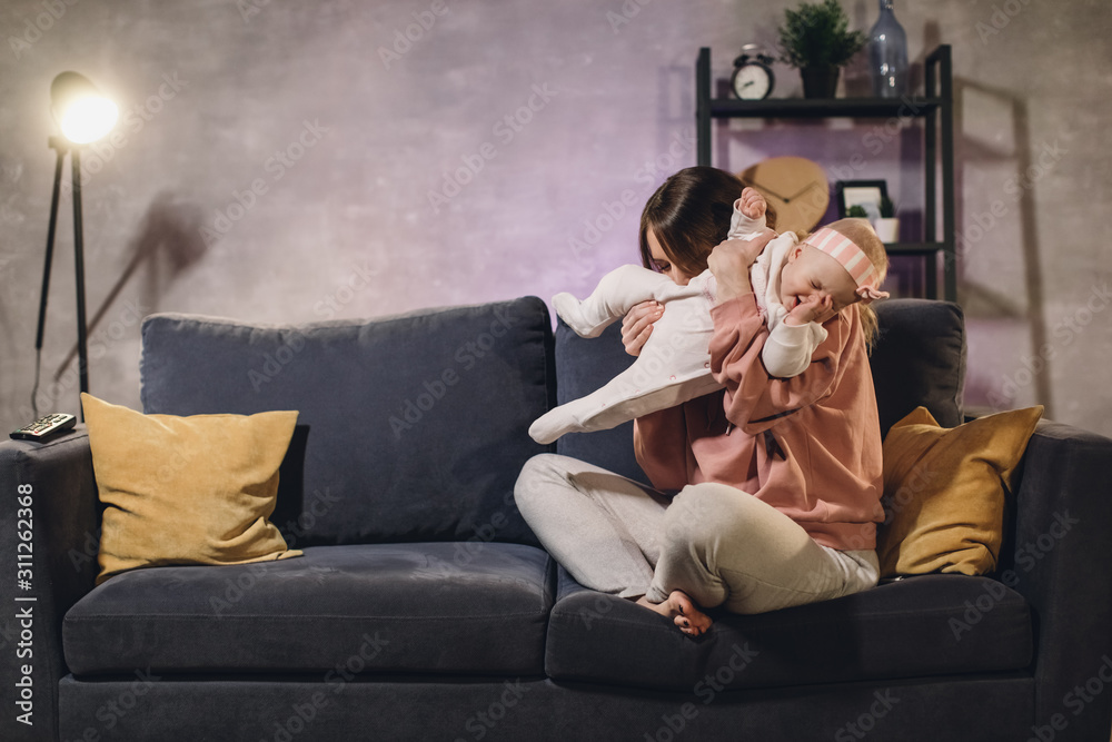 A woman plays with her child on the couch in a cozy apartment. Mom and baby are happy A woman plays with her child on the couch in a cozy apartment. Mom and baby are happy