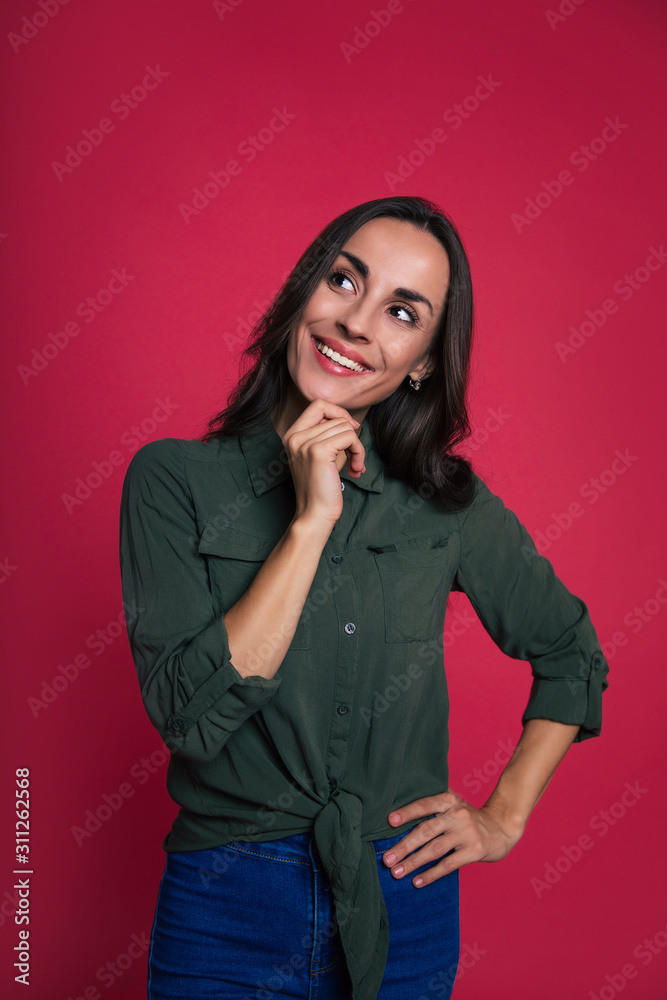 Think and smile. Close-up photo of a casually dressed gorgeous woman with wavy hair, who is holding her chin with her right hand, smiling and looking to the left with curiosity. Think and smile. Close-up photo of a casually dressed gorgeous woman with wavy hair, who is holding her chin with her right hand, smiling and looking to the left with curiosity.