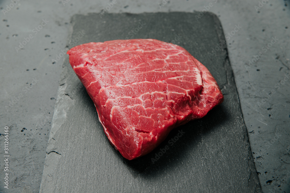 Raw beef, beef steak on a stone background. The concept of preparing a meal and eating. Fresh red beef, preparing a steak, using meat with a meal.