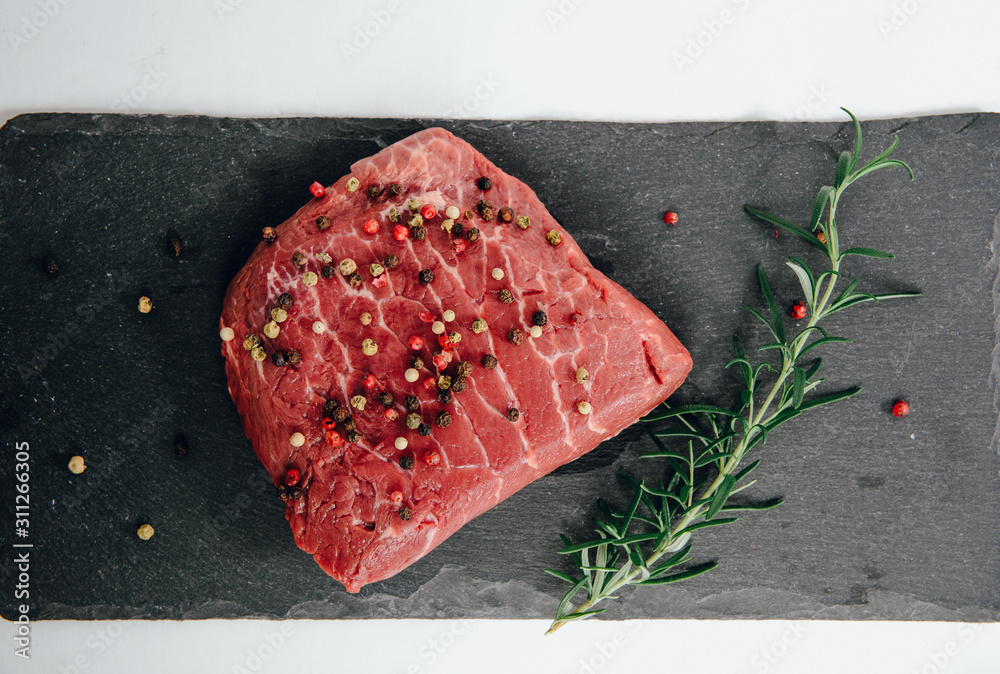 Raw beef, beef steak on a white isolated background with rosemary and spices. The concept of preparing a meal and eating. Fresh red beef, preparing a steak, using meat with a meal.
