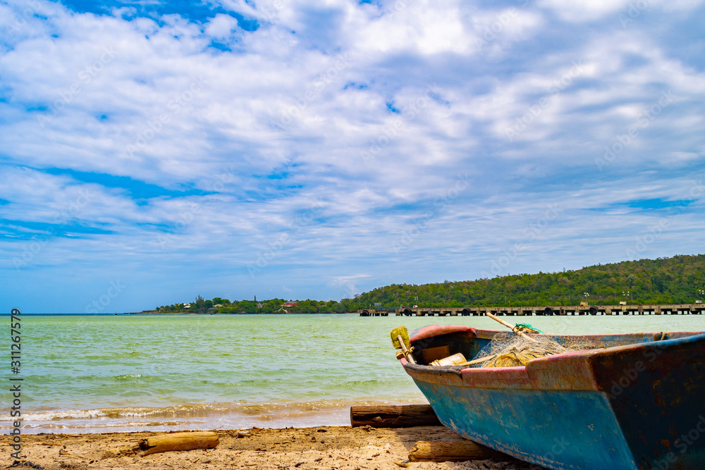 Old blue wooden fishing boat docked on sea shore/ seashore on white sand beach coast landscape with empty fish nets and paddles mounted/ rolled on a log. Sunny summer day on tropical Caribbean island. Old blue wooden fishing boat docked on sea shore/ seashore on white sand beach coast landscape with empty fish nets and paddles mounted/ rolled on a log. Sunny summer day on tropical Caribbean island.