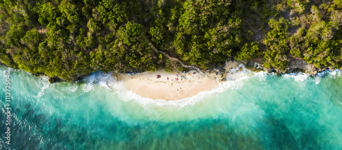 View from above, stunning aerial view of some tourists sunbathing on a beautiful beach bathed by a turquoise rough sea during sunset, Green Bowl Beach, South Bali, Indonesia.