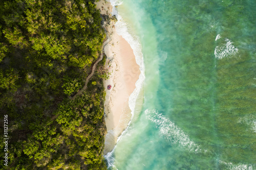 Fototapeta Naklejka Na Ścianę i Meble -  View from above, stunning aerial view of some tourists sunbathing on a beautiful beach bathed by a turquoise rough sea during sunset, Green Bowl Beach, South Bali, Indonesia.