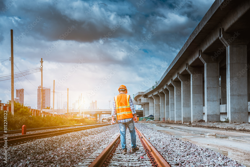 Naklejka premium A senior engineer under inspection and checking construction process railway and checking work on railroad station platform .Engineer wearing safety uniform and safety helmet in work.