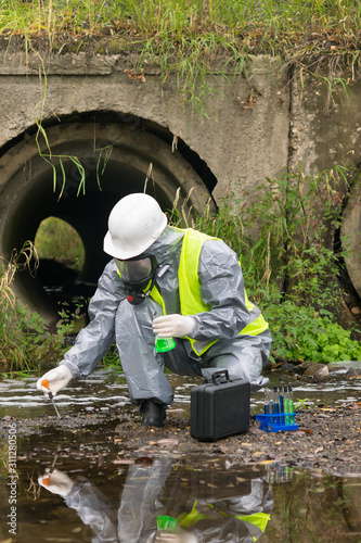 an employee in a protective suit and mask takes water from the river with a pipette and conducts a test of the suitability of water after a man-made disaster © kurgu128