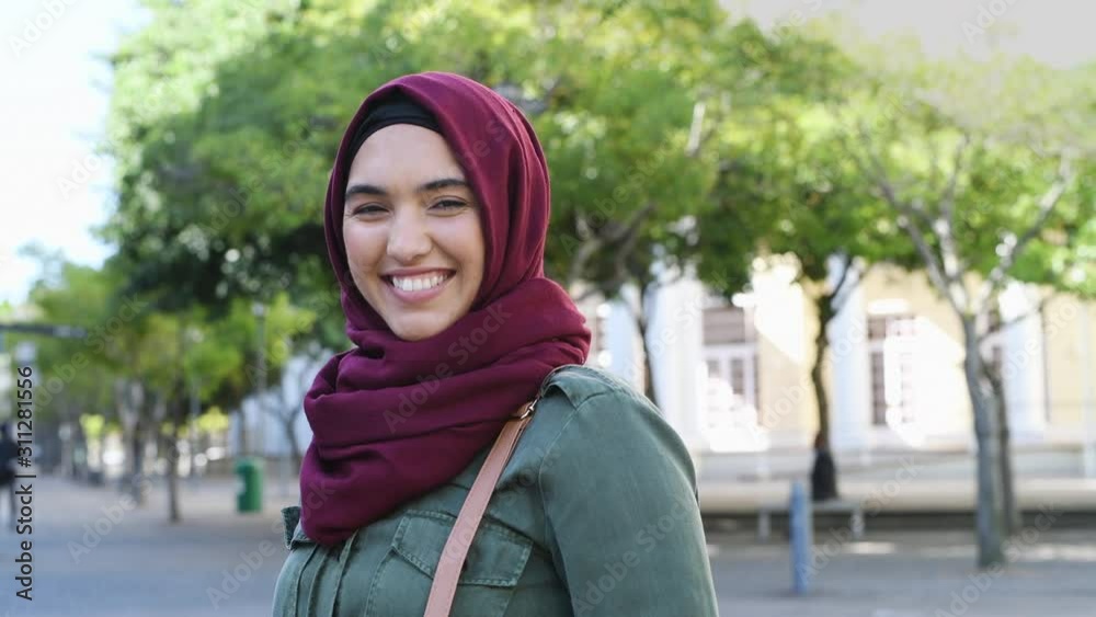 Portrait of young muslim woman wearing hijab head scarf in city while looking at camera. Closeup face of cheerful woman covered with headscarf smiling outdoor. Casual islamic girl at park. Portrait of young muslim woman wearing hijab head scarf in city while looking at camera. Closeup face of cheerful woman covered with headscarf smiling outdoor. Casual islamic girl at park.