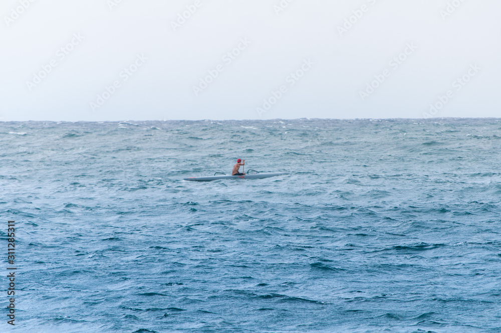 A single kayak-er paddles in the ocean off the coast of Maui Hawaii. Photo taken in a horizontal, landscape orientation 