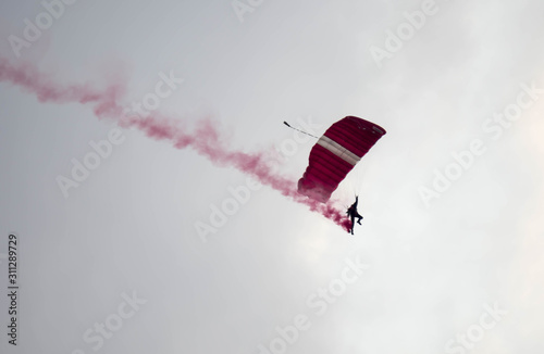 silhouette parachute stunt unfocused and blurry while gliding in the air with red smoke trail during an air exhibition