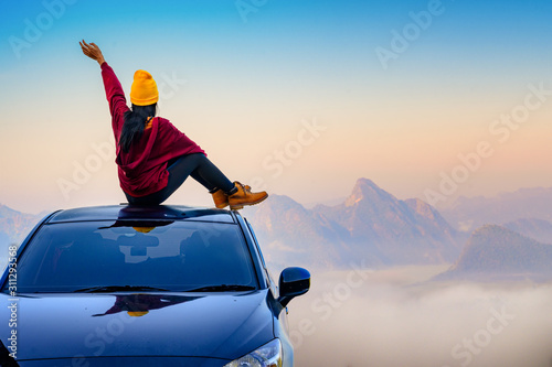 young woman sitting on the car roof with enjoy the nature of mist in the mountain at sunrise morning, opening arm cheerfully life