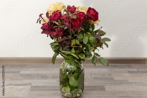 Roses flowers in a glass jar on the floor against a white wall