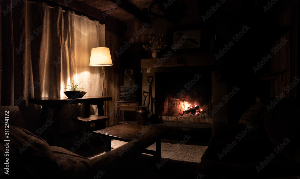 Interior of a wooden cozy and relaxing cabin with comfortable couches, country decoration, dimly lit by the fireplace and lamp. Concept of silence, tranquility, time to rest and relaxation. Interior of a wooden cozy and relaxing cabin with comfortable couches, country decoration, dimly lit by the fireplace and lamp. Concept of silence, tranquility, time to rest and relaxation.