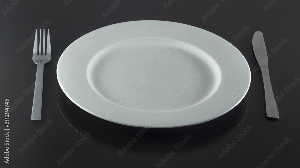 empty white plate with knife and fork on a shiny surface