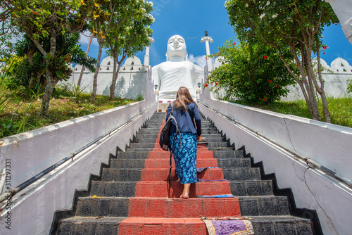 Tableau sur toile Back view of young tourist woman visit the white giant Buddha statue in Sri Maha Bodhi Viharaya located on the top of small hill in Kandy city, Sri Lanka