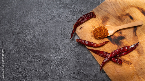 Cayenne pepper in a wooden spoon and dried chillies placed on a wooden chopping board on the cement floor