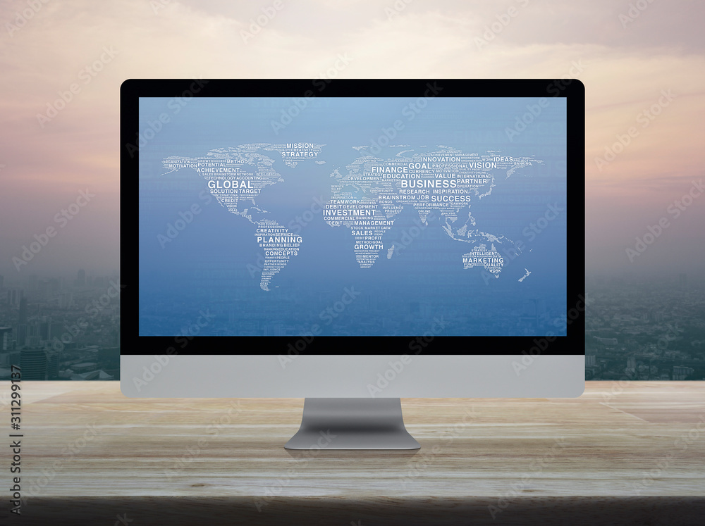 Fototapeta premium Global business words world map on desktop modern computer monitor screen on wooden table over city tower and skyscraper at sunset sky, vintage style, Global business online concept, Elements of this 