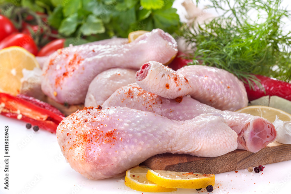 Fresh chicken legs with tomatoes, lemon and spices, on a white background