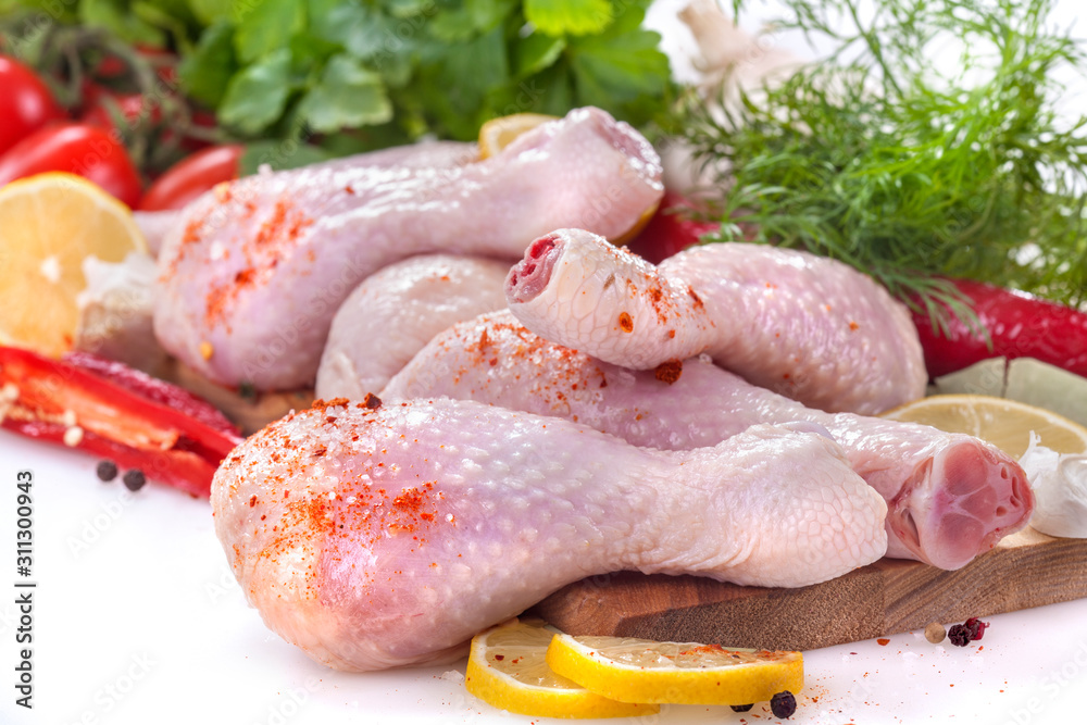 Fresh chicken legs with tomatoes, lemon and spices, on a white background Fresh chicken legs with tomatoes, lemon and spices, on a white background