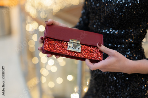 Red little female clutch bag with sequins. Brilliant, festive for a party. girl in a black dress holds in her hands. Accessories for a female image photo