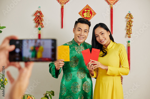 Beautiful young couple celebrating Lunar New Year and showing traditional red and yellow paper envelopes