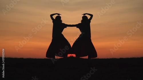 Mirror image of a bohemian dancers silhouette at sunset. The twin dancers flow against the fiery orange horizon.