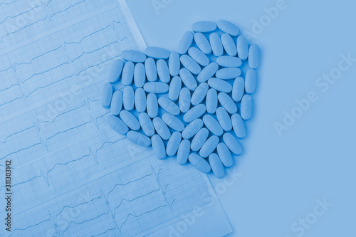 Cardiogram with red heart made from pills (tablets) on a classic blue background close up, with copy space for text. Cardiological care. Cardiology, medical and insurance concept.