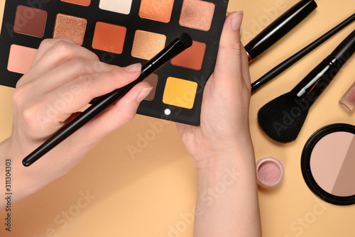 Eye shadow palette on woman hand. Professional makeup products with cosmetic beauty products, foundation, lipstick, eye shadows, brushes and tools.